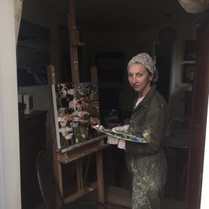 Artist standing in front of an easel dressed in paint-covered overalls